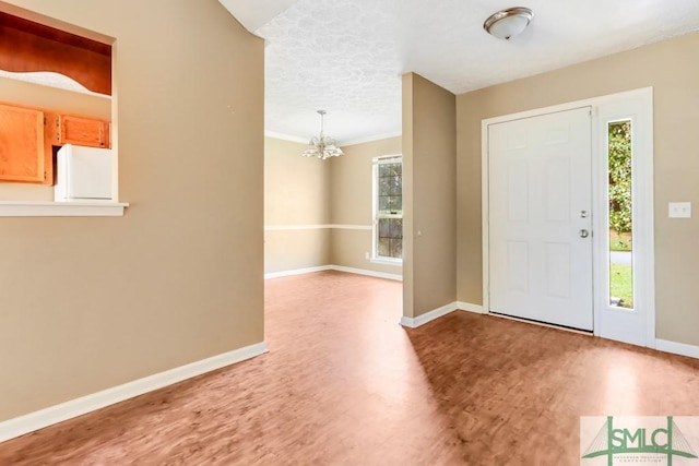 foyer entrance featuring a notable chandelier, ornamental molding, wood finished floors, and baseboards