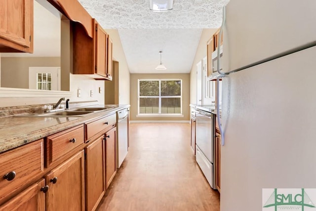 kitchen with a textured ceiling, white appliances, a sink, light countertops, and brown cabinetry