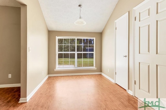 interior space with light wood-type flooring, baseboards, vaulted ceiling, and a textured ceiling