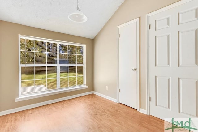 interior space featuring light wood finished floors, baseboards, vaulted ceiling, and a textured ceiling