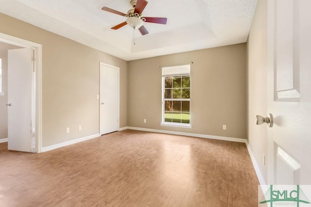 unfurnished room with ceiling fan, a tray ceiling, wood finished floors, and baseboards