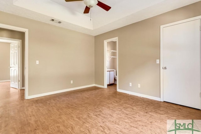 unfurnished bedroom featuring light wood-style floors, a tray ceiling, visible vents, and baseboards