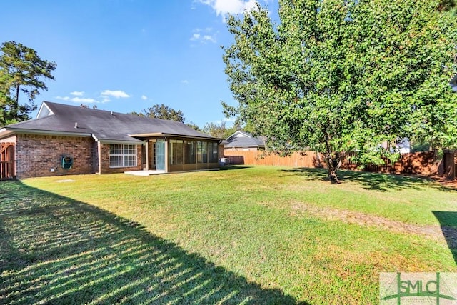 rear view of house featuring a yard, brick siding, a fenced backyard, and a sunroom