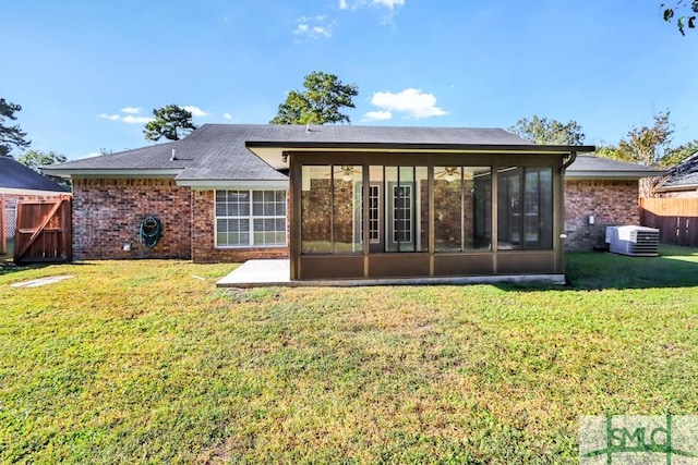 rear view of house with a lawn, a sunroom, fence, central AC, and brick siding