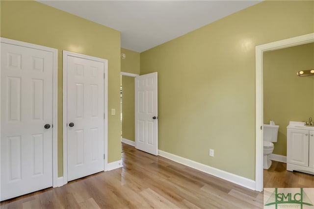 unfurnished bedroom featuring ensuite bath and light hardwood / wood-style flooring