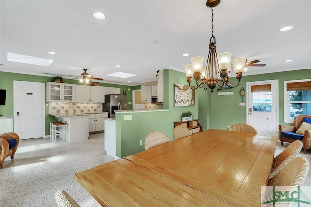 dining space with crown molding, ceiling fan with notable chandelier, and a skylight