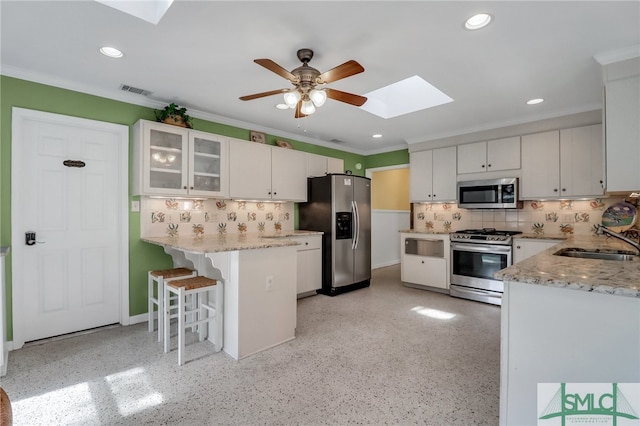 kitchen with stainless steel appliances, sink, a breakfast bar area, a skylight, and white cabinetry