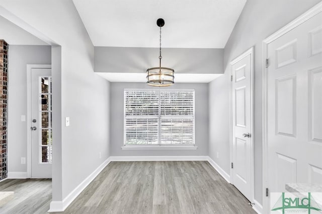 unfurnished dining area with light hardwood / wood-style flooring, lofted ceiling, and a notable chandelier