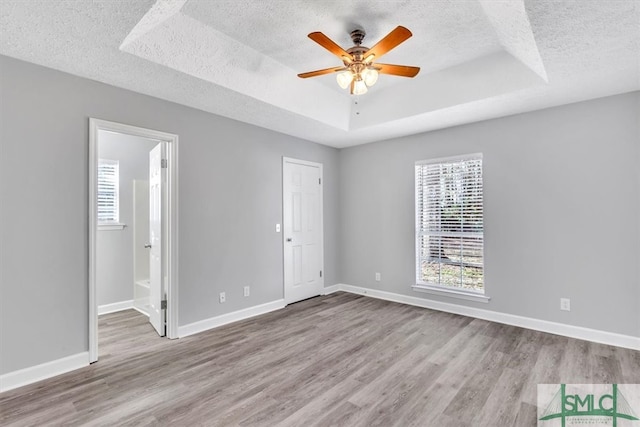 unfurnished bedroom with a textured ceiling, connected bathroom, ceiling fan, a raised ceiling, and light wood-type flooring