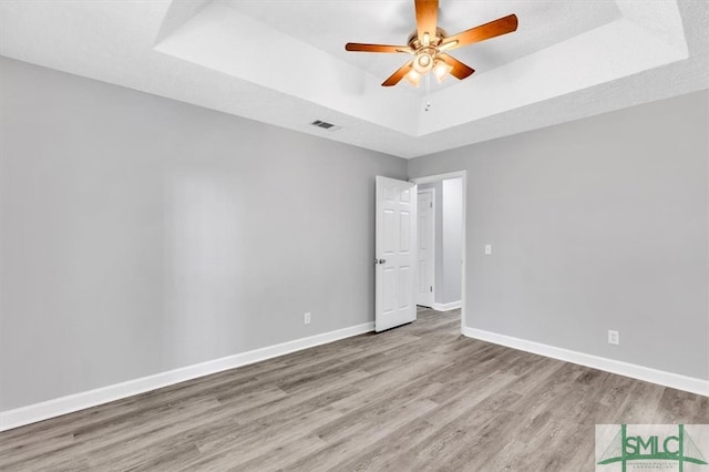 empty room featuring a tray ceiling, ceiling fan, and light hardwood / wood-style flooring