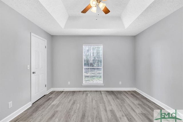 spare room with a textured ceiling, light hardwood / wood-style flooring, and a tray ceiling