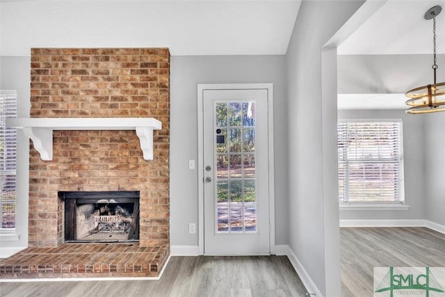 unfurnished living room featuring an inviting chandelier, vaulted ceiling, hardwood / wood-style flooring, and a brick fireplace