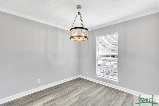 empty room featuring wood-type flooring, ornamental molding, a textured ceiling, and a notable chandelier