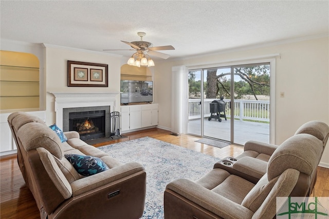 living room featuring a textured ceiling, a fireplace, ceiling fan, crown molding, and light wood-type flooring