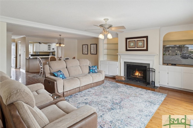 living room with ornamental molding, ceiling fan with notable chandelier, light hardwood / wood-style flooring, and a tile fireplace