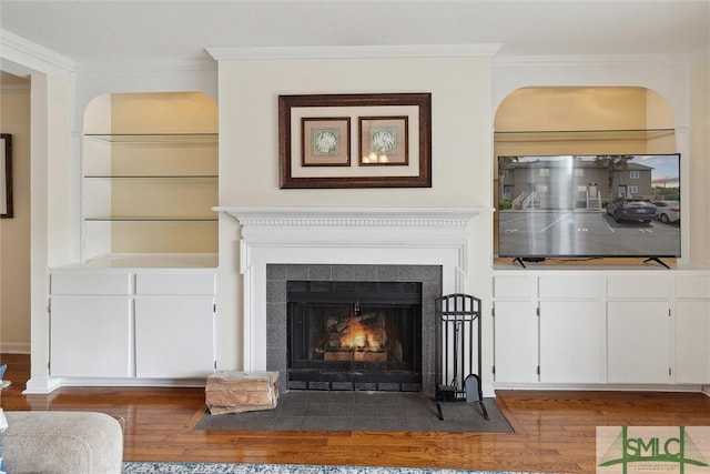 unfurnished living room featuring dark wood-type flooring, crown molding, and a tile fireplace