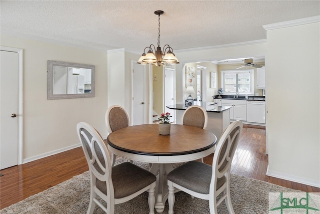 dining room with sink, ornamental molding, ceiling fan with notable chandelier, a textured ceiling, and dark hardwood / wood-style flooring