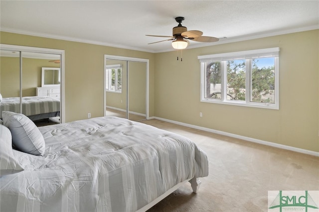 bedroom featuring ceiling fan, multiple windows, light carpet, and two closets