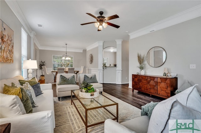 living room featuring dark hardwood / wood-style flooring, decorative columns, ornamental molding, and ceiling fan with notable chandelier