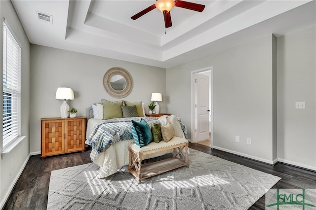 bedroom with ceiling fan, dark hardwood / wood-style floors, multiple windows, and a raised ceiling