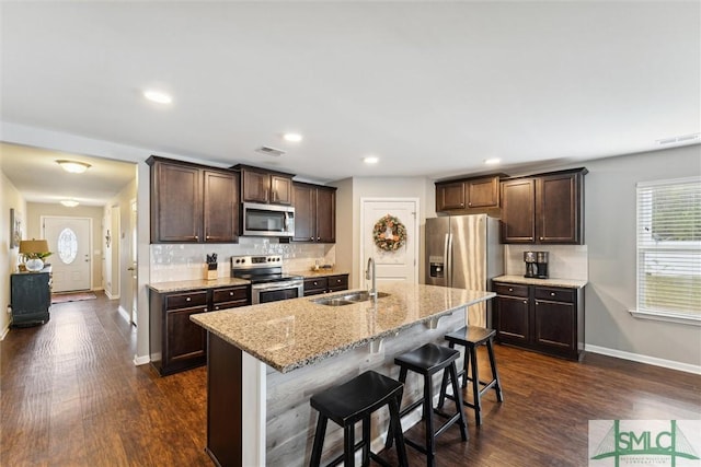 kitchen featuring a center island with sink, stainless steel appliances, light stone counters, a breakfast bar, and sink