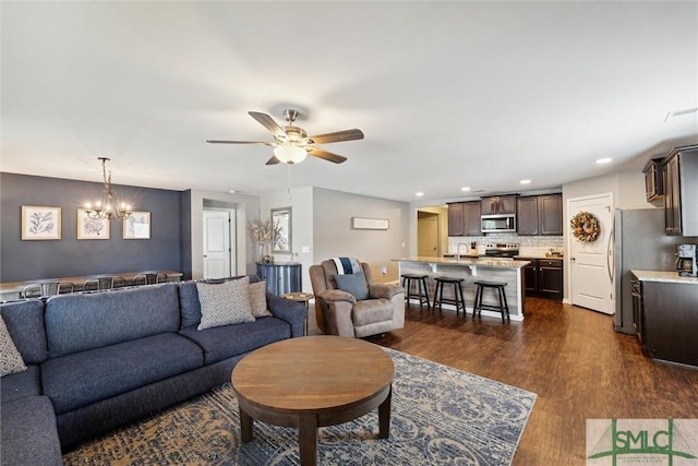 living room with ceiling fan with notable chandelier, sink, and dark hardwood / wood-style flooring