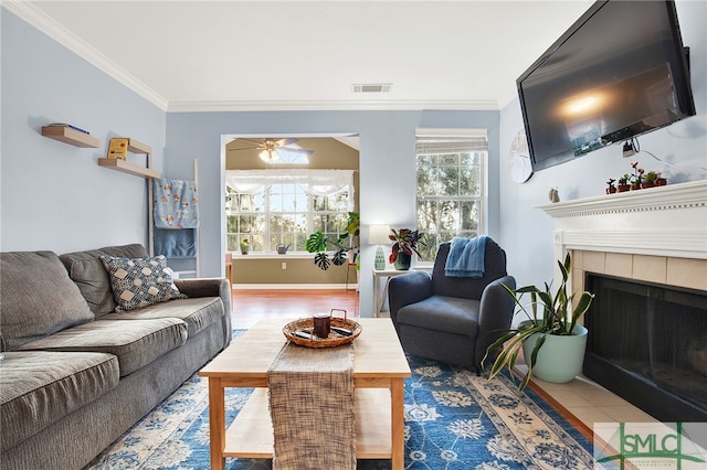 tiled living room with ceiling fan, a tile fireplace, and crown molding