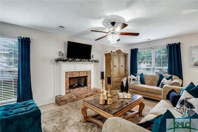 living room featuring a brick fireplace, ceiling fan, and a textured ceiling