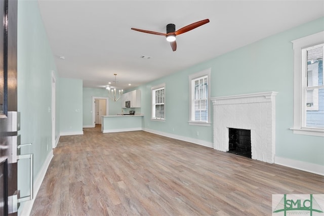 unfurnished living room featuring a brick fireplace, a healthy amount of sunlight, and light hardwood / wood-style flooring