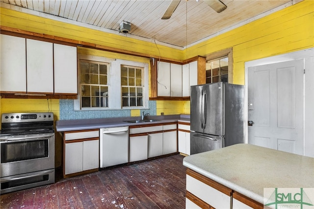 kitchen with stainless steel appliances, sink, dark hardwood / wood-style floors, white cabinets, and wooden walls