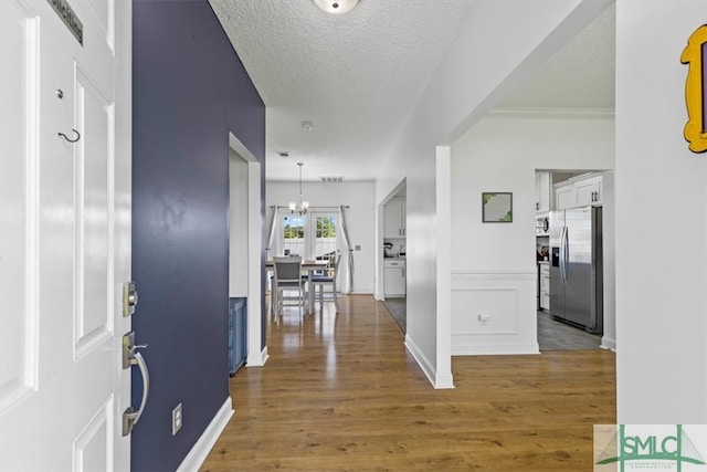 foyer entrance featuring a textured ceiling, ornamental molding, hardwood / wood-style flooring, and a chandelier