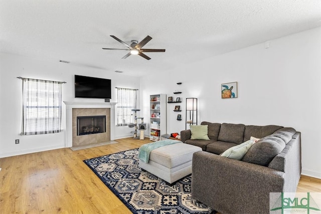 living room with wood-type flooring, a tile fireplace, ceiling fan, and a textured ceiling