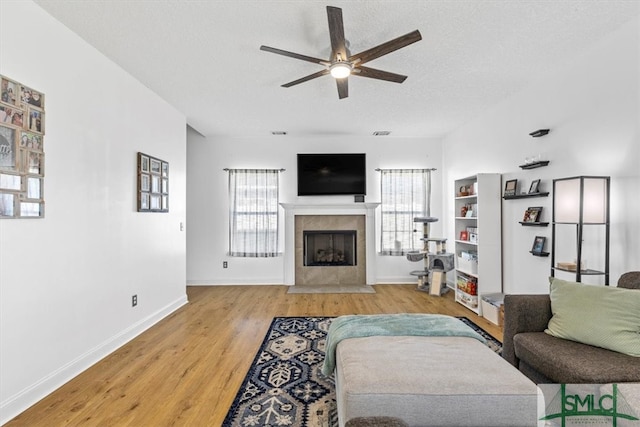 living room featuring ceiling fan, a textured ceiling, a tile fireplace, and light hardwood / wood-style floors