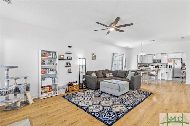 living room with ceiling fan with notable chandelier, light hardwood / wood-style flooring, and a textured ceiling