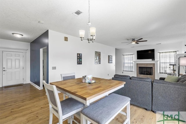 dining area featuring hardwood / wood-style flooring, ceiling fan with notable chandelier, a tile fireplace, and a textured ceiling