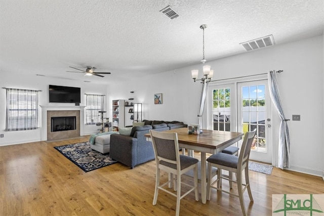 dining room featuring light wood-type flooring, ceiling fan with notable chandelier, and a textured ceiling