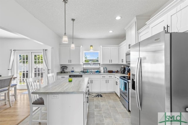 kitchen featuring white cabinetry, appliances with stainless steel finishes, hanging light fixtures, and a kitchen island