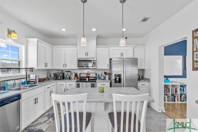 kitchen with a textured ceiling, sink, decorative light fixtures, and stainless steel appliances