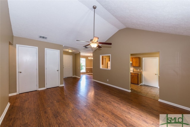 unfurnished living room with a textured ceiling, dark hardwood / wood-style floors, vaulted ceiling, and ceiling fan