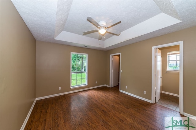 unfurnished bedroom featuring a raised ceiling, multiple windows, and dark wood-type flooring