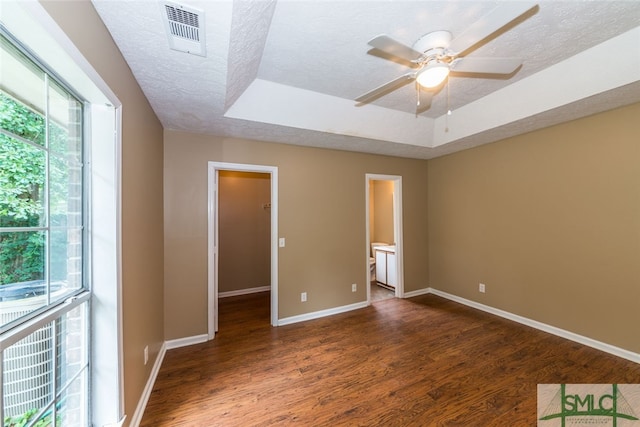 unfurnished bedroom featuring dark hardwood / wood-style flooring, a walk in closet, a raised ceiling, ceiling fan, and connected bathroom