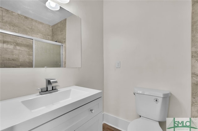 bathroom featuring toilet, vanity, and a shower with shower door