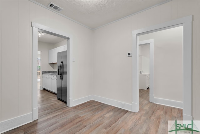 empty room featuring light wood-type flooring, a textured ceiling, and ornamental molding