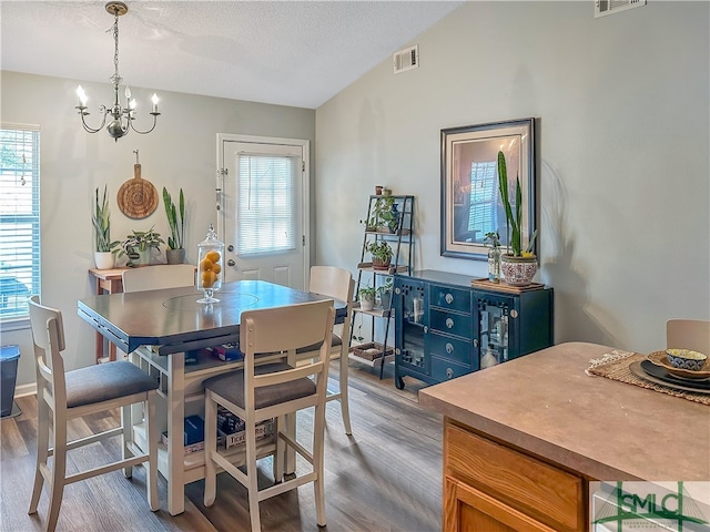 dining area featuring an inviting chandelier, lofted ceiling, a textured ceiling, and light hardwood / wood-style floors