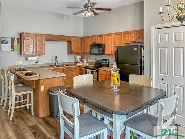 kitchen featuring ceiling fan with notable chandelier, dark wood-type flooring, black appliances, sink, and a kitchen breakfast bar