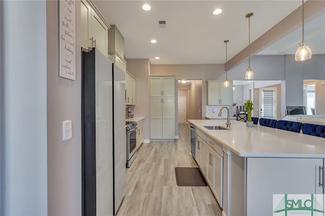 kitchen with a center island with sink, sink, appliances with stainless steel finishes, pendant lighting, and light wood-type flooring