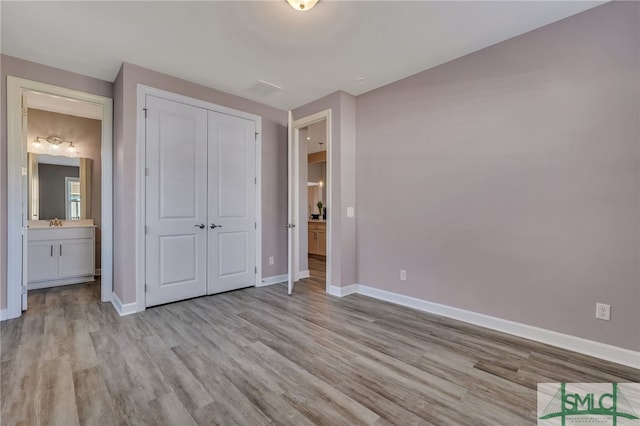 unfurnished bedroom featuring connected bathroom, a closet, sink, and light hardwood / wood-style flooring