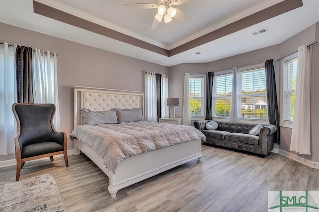 bedroom with ornamental molding, light hardwood / wood-style floors, ceiling fan, and a tray ceiling