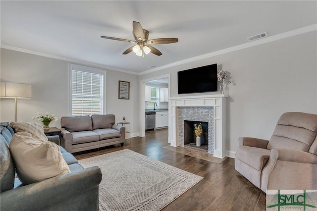 living room featuring dark hardwood / wood-style floors, ceiling fan, ornamental molding, and a tiled fireplace