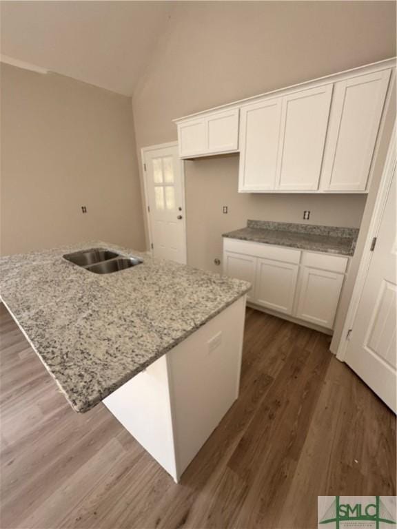 kitchen with hardwood / wood-style floors, lofted ceiling, white cabinets, light stone countertops, and an island with sink